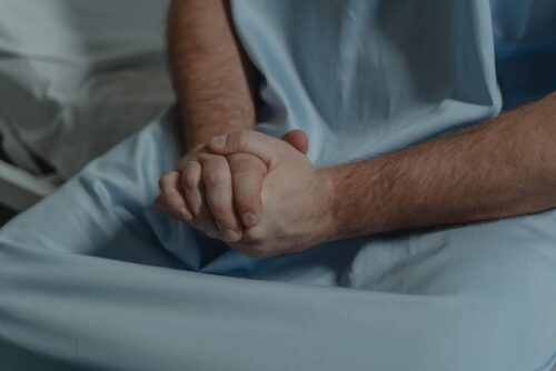 person in hospital gown with hands clasped