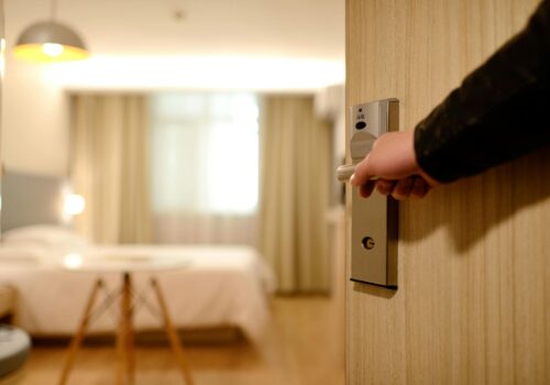 A person’s hand opens a hotel room door, revealing a bright, modern room with a neatly made bed—highlighting the importance of hotel liability MD in ensuring guest safety and comfort.