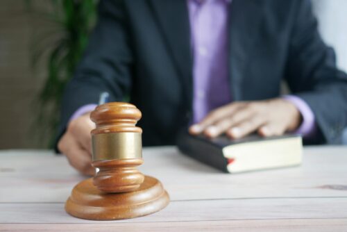 A person in a suit sits at a desk, holding a book with one hand while a wooden judge's gavel rests on the table, suggesting legal action for injuries caused by a defective home appliance in MD.
