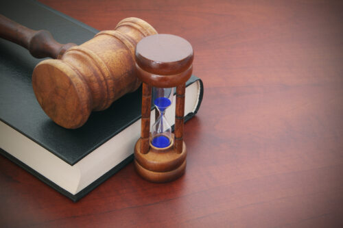 A wooden gavel rests on a closed book beside an hourglass with blue sand, set on polished wood—a classic symbol for those looking to file a claim in Maryland, even if the accident happened months ago.