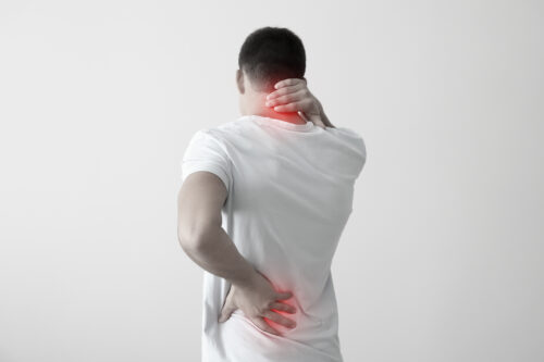 A person stands facing away, holding their neck and lower back with one hand each, showing pain possibly from a Maryland car accident that could worsen a pre-existing condition. Red highlights mark discomfort; the background is plain and light-colored.